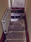 Interior photograph showing a narrow stone staircase with a white radiator on the left wall leading to a door with patterned glass.