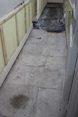 A narrow outdoor side passage paved with large stone slabs, flanked by a wall with pale yellow cladding on the left and a white wall on the right.