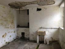 An interior photograph of a dilapidated room featuring peeling paint, a damaged ceiling with exposed lath, and a stone sink.