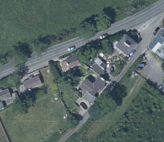 Aerial satellite view of a rural property showing a main house, outbuildings, and a nearby road.