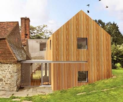 A photorealistic architectural rendering showing a modern timber-clad extension attached to an existing stone building with a tiled roof.