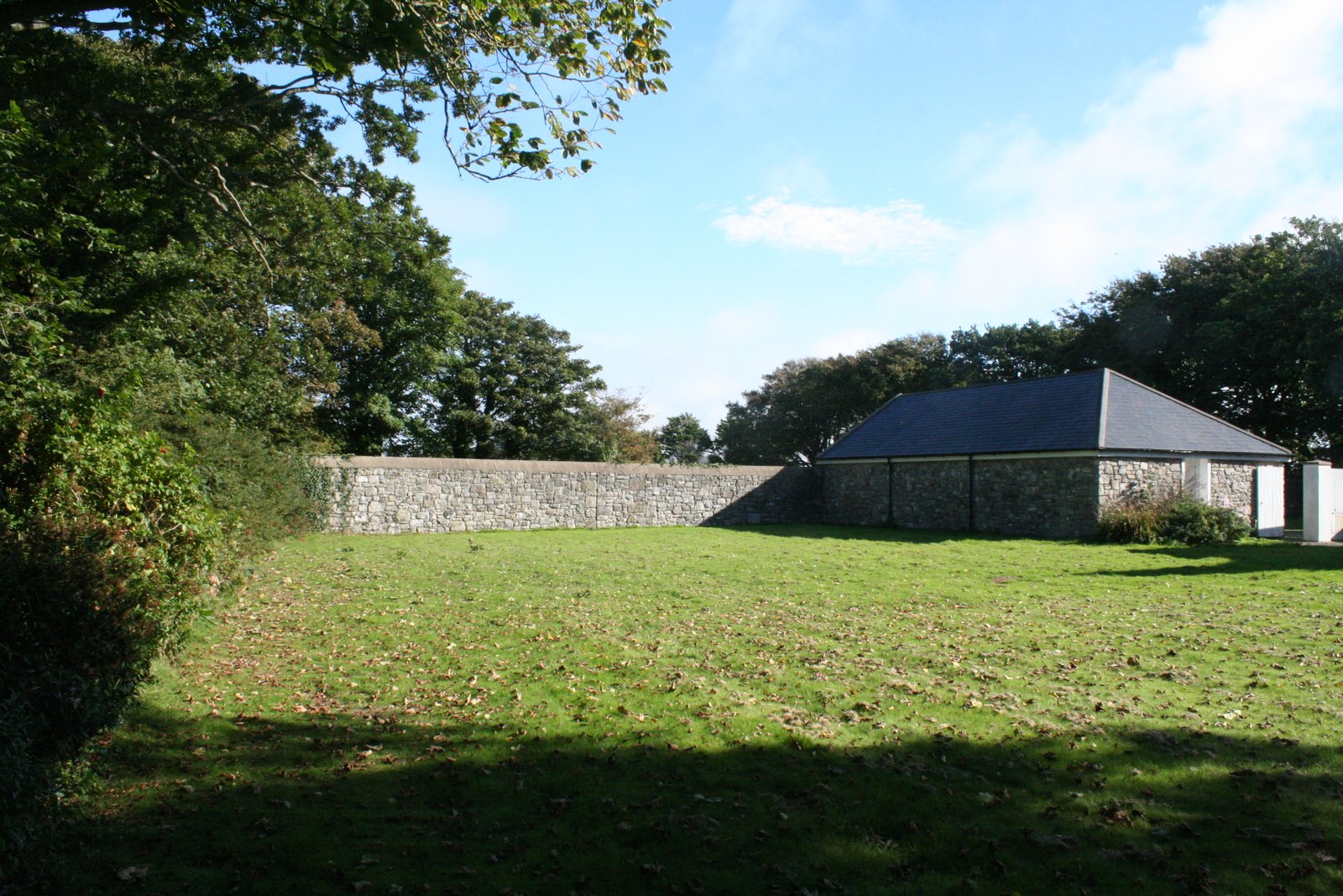 A photograph showing a grassy garden area with a stone boundary wall and a stone outbuilding in the background.