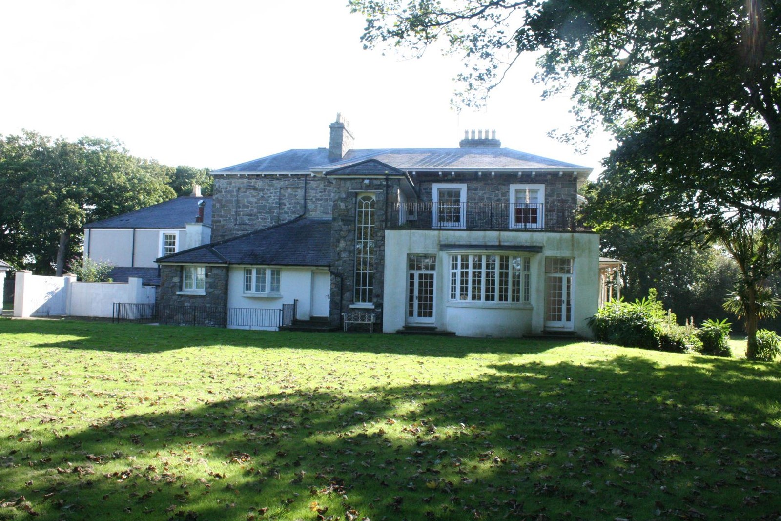 A photograph showing a large detached stone house with a spacious grassy garden and mature trees.