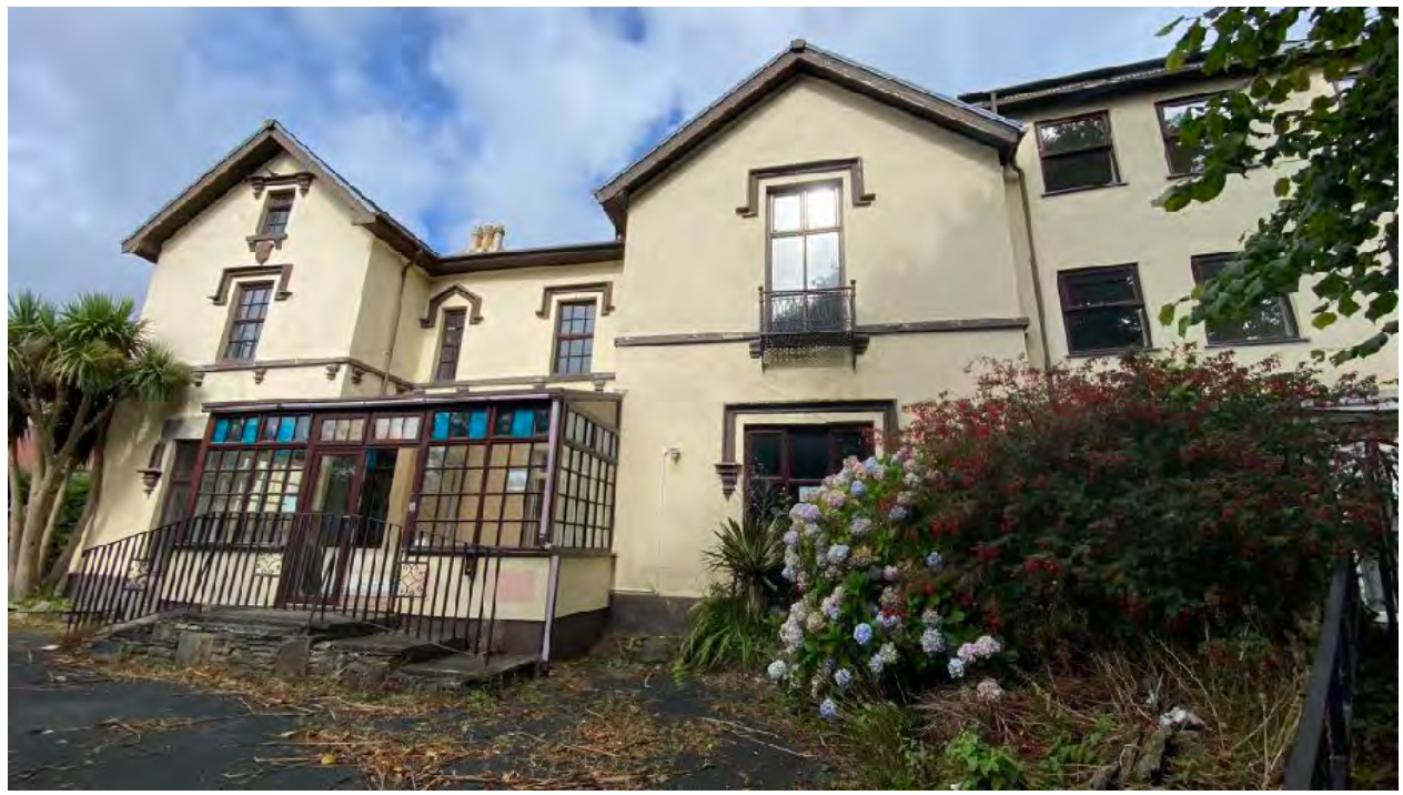 A photograph of a large, cream-colored detached building with a conservatory extension and balcony, likely the former nursing home to be demolished.