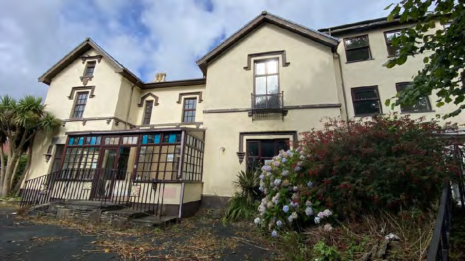 A photograph of a large, cream-colored building with a conservatory extension, likely the former nursing home proposed for demolition.