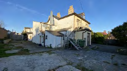 A photograph showing the existing white building and attached single-story outbuilding with an external metal staircase, which are the subject of the demolition application.