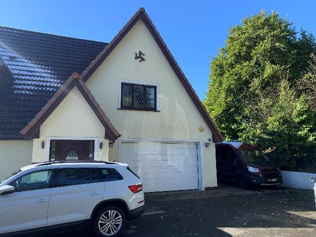 A photograph of a detached house featuring a cream-colored exterior, a white garage door, and a driveway with parked vehicles.