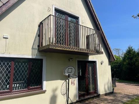 A photograph showing the exterior elevation of a two-story detached house featuring a balcony, windows with security grilles, and a basketball hoop in the driveway.