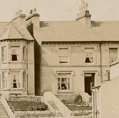 A sepia-toned historical photograph showing the front elevation of a large two-story detached house with a prominent bay window and stone steps leading to the entrance.