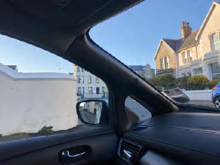 A photograph taken from inside a vehicle looking out at a residential street featuring detached and terraced houses.