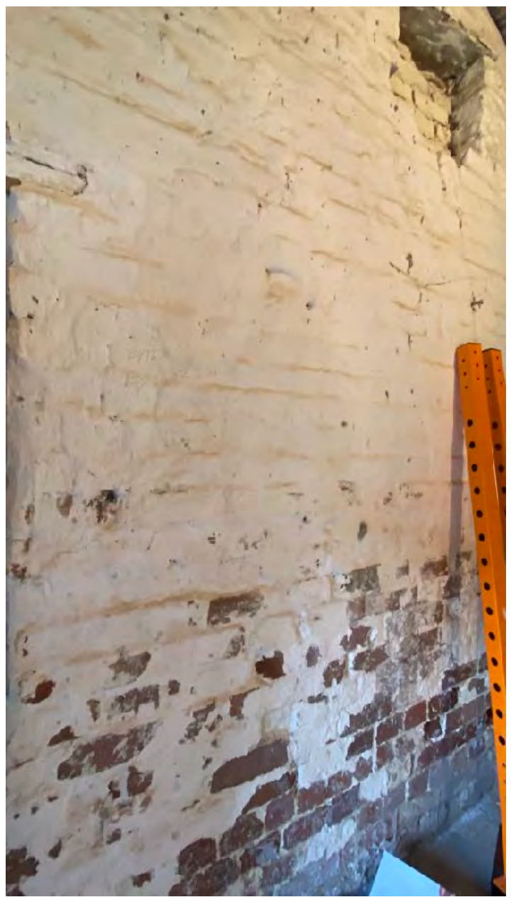 A close-up photograph showing the interior of a weathered brick wall with peeling white paint and an orange metal shelving unit leaning against it.