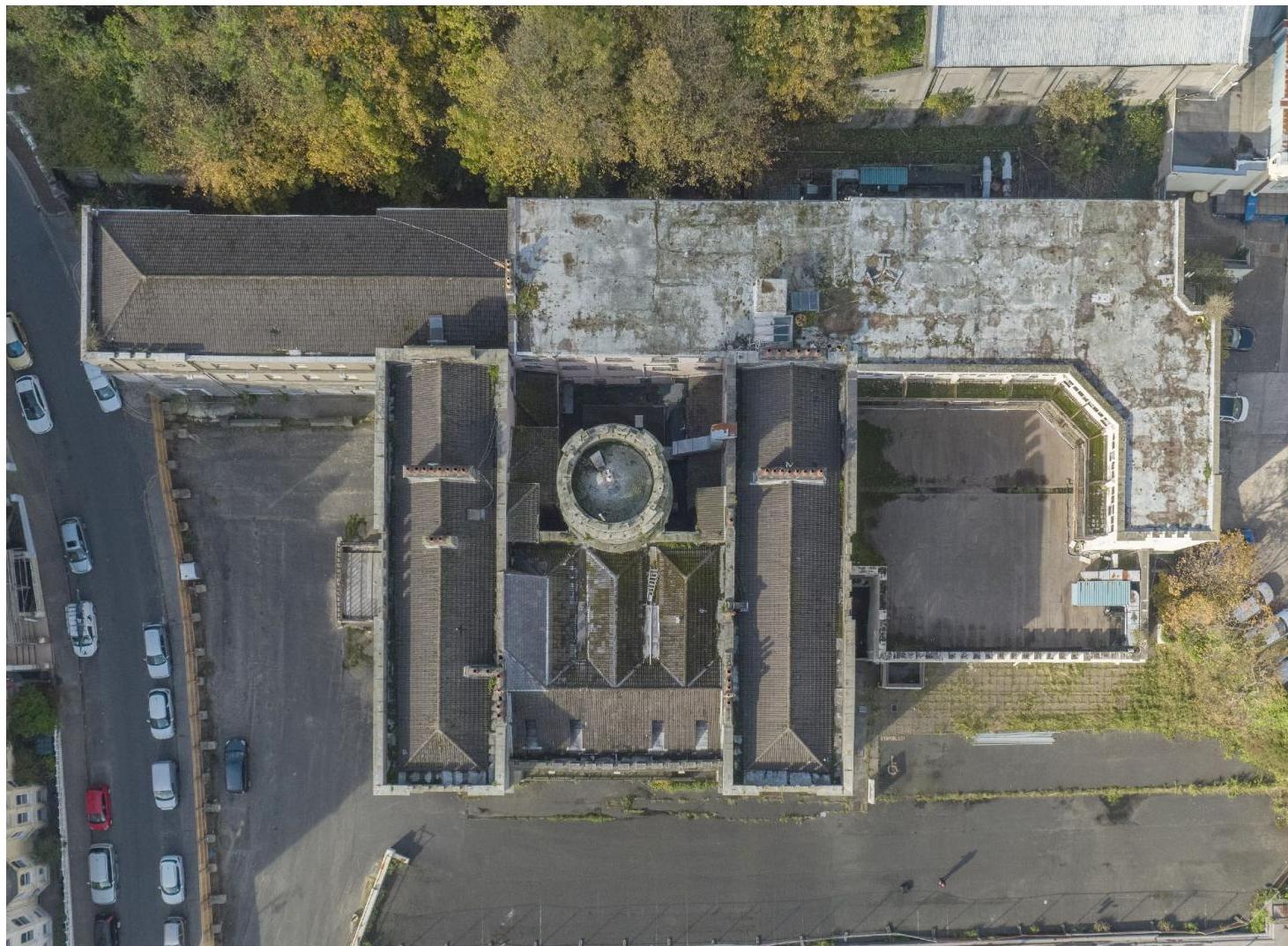 An aerial photograph showing the roof layout of a large, historic building complex with a central circular feature and surrounding paved areas.