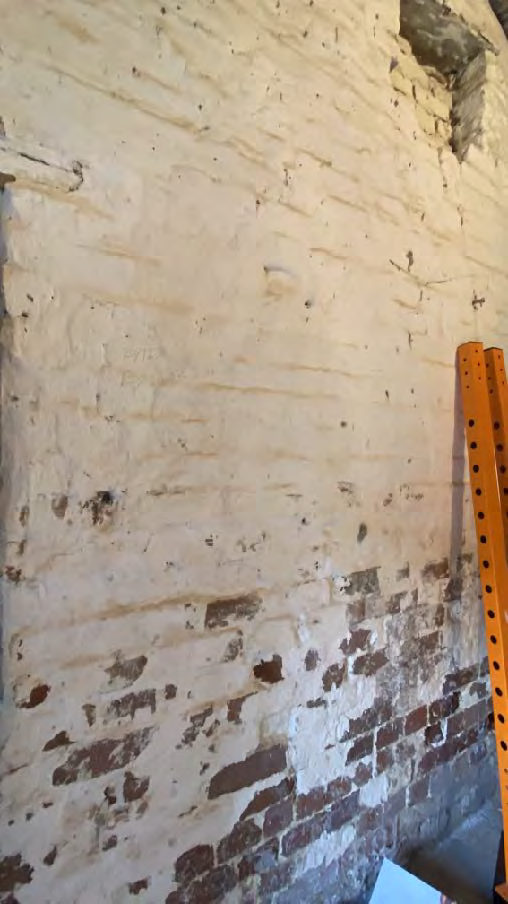 A close-up photograph showing the interior of a brick wall with peeling white paint, revealing the underlying masonry.
