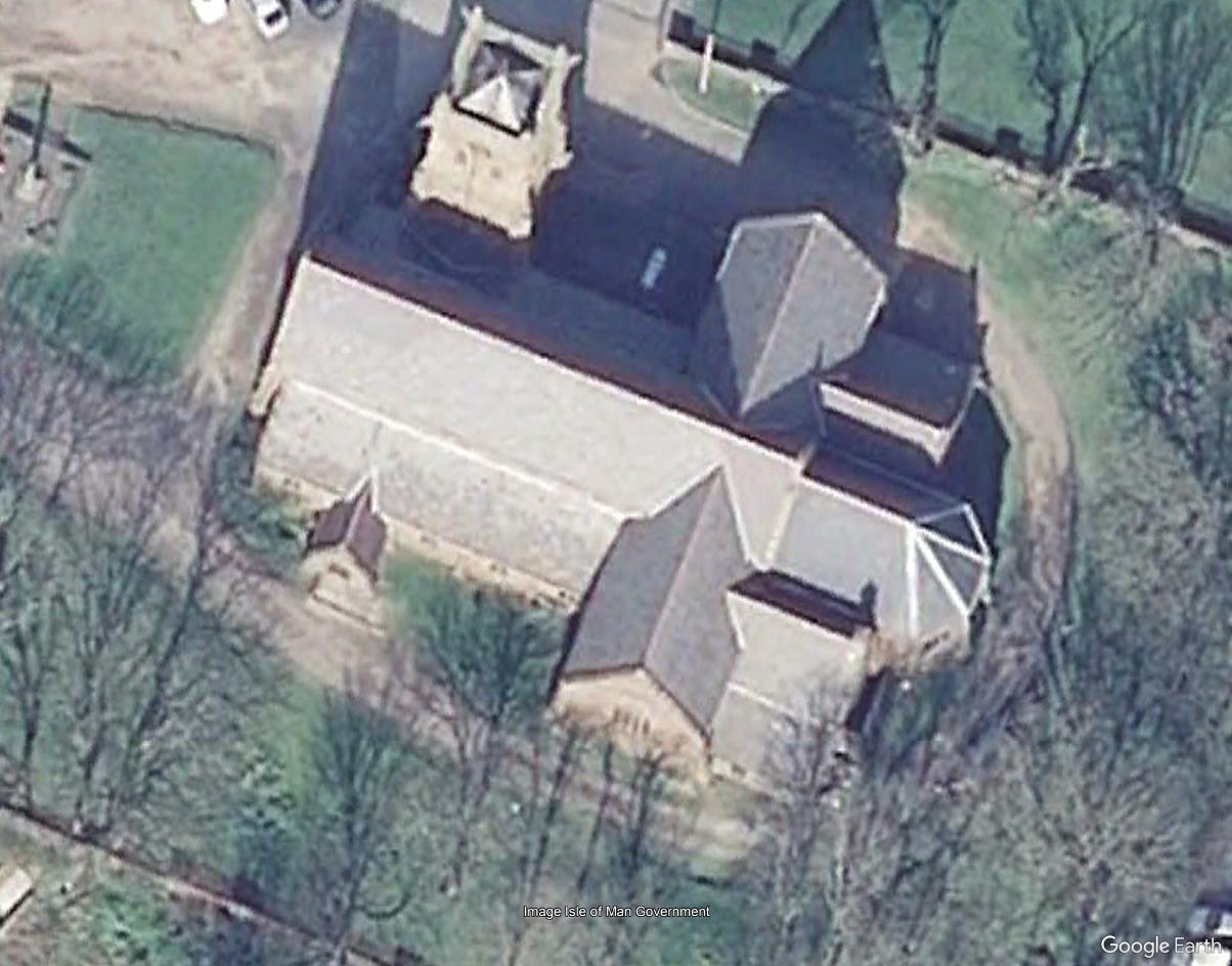 An aerial satellite view of a large stone building with a pitched roof and tower, surrounded by trees and a driveway.