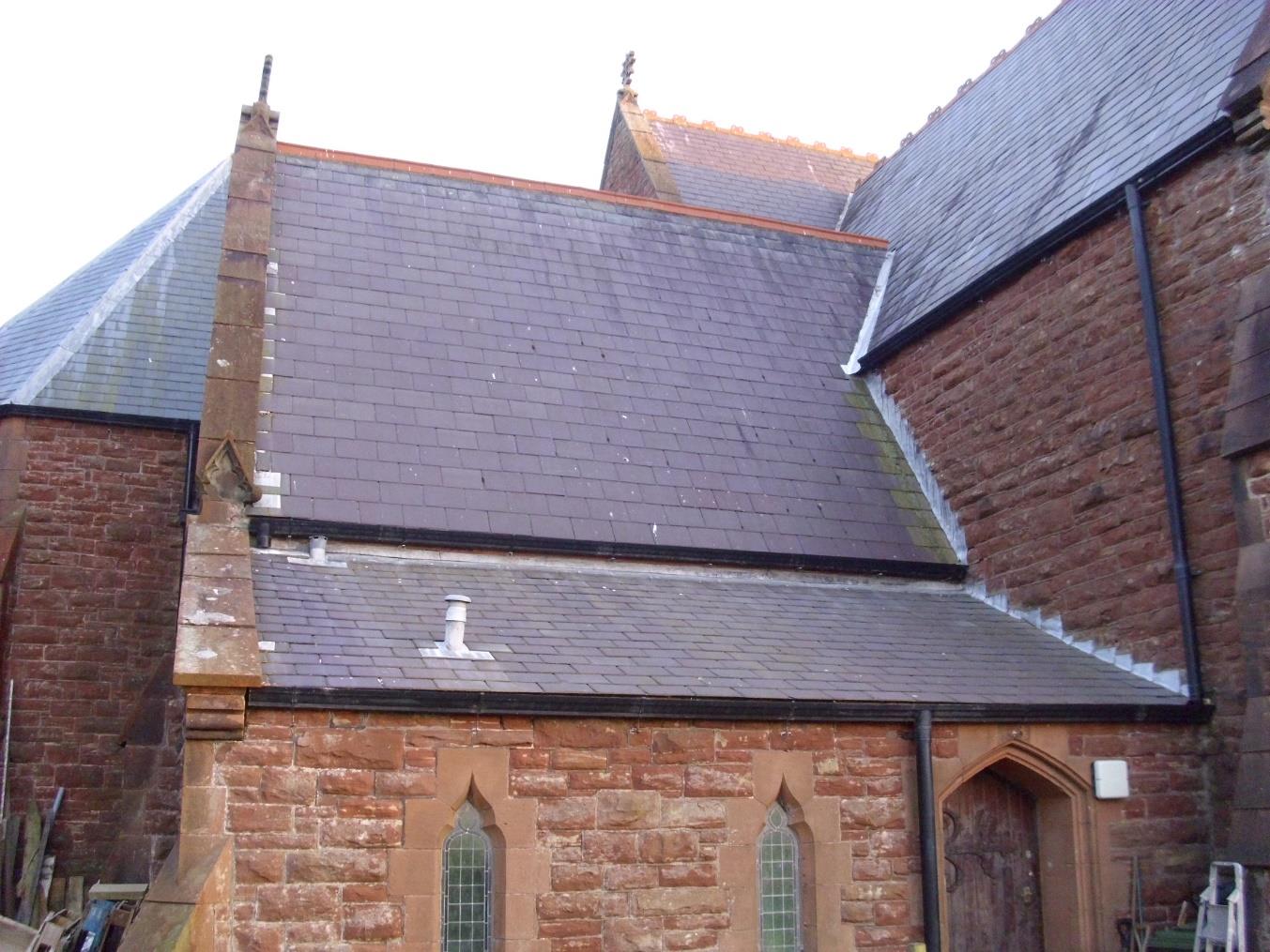 A photograph showing the exterior elevation of a red sandstone building with a slate roof, featuring arched windows and a chimney stack, likely a church or chapel.