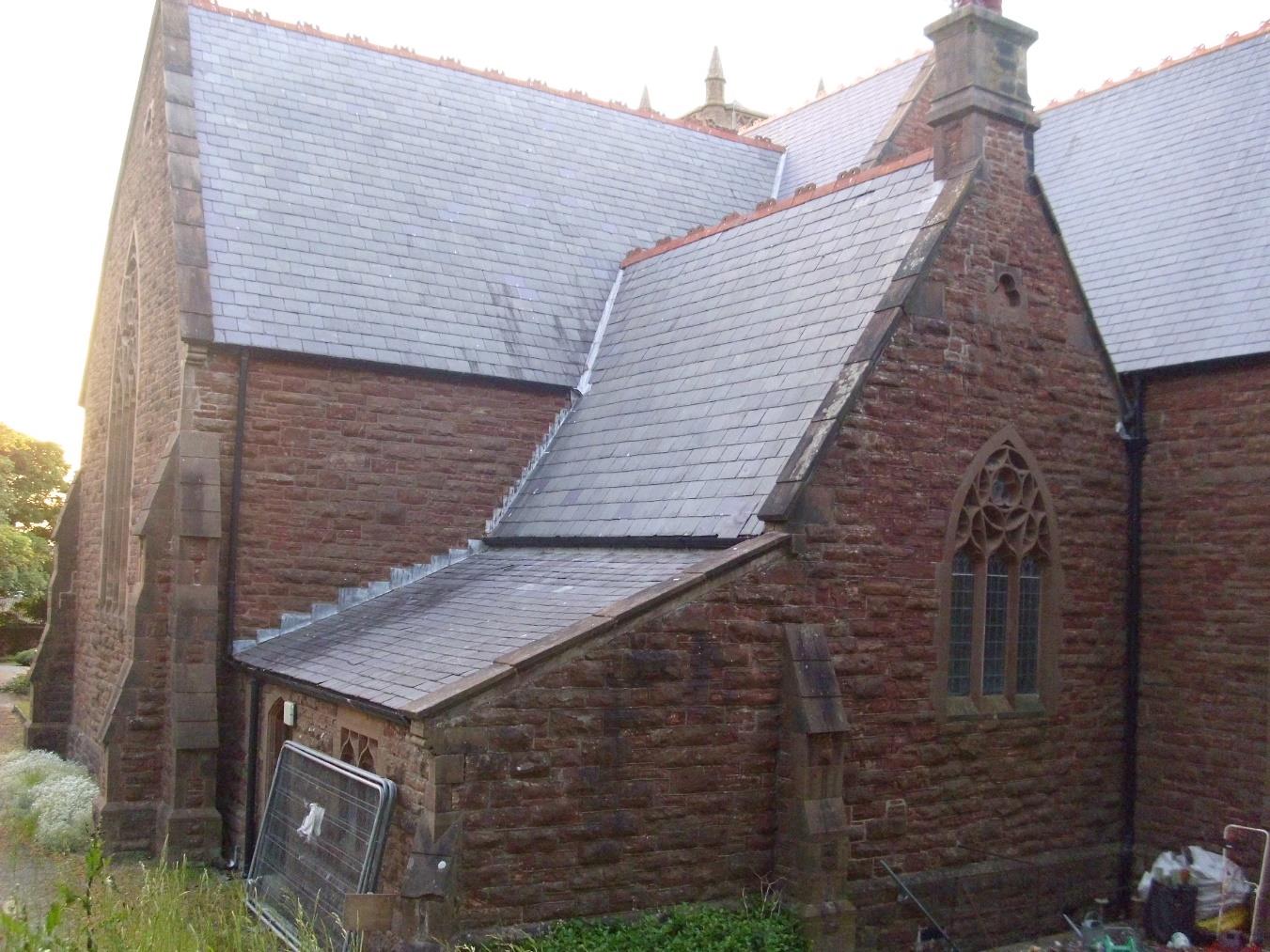 An exterior photograph of a large stone building, likely a church or chapel, featuring slate roofing and Gothic-style windows.