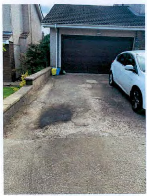 A photograph showing a residential driveway leading to a garage with a white car parked on the right side.