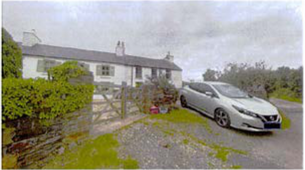A photograph showing a white, two-story detached house with a slate roof and a gravel driveway with a silver car parked on it.
