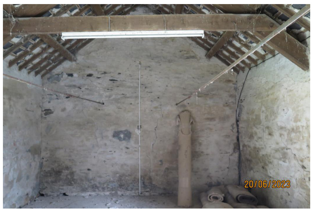 Interior photograph of a rustic room with exposed wooden roof beams and rough plastered walls, likely part of a barn conversion project.