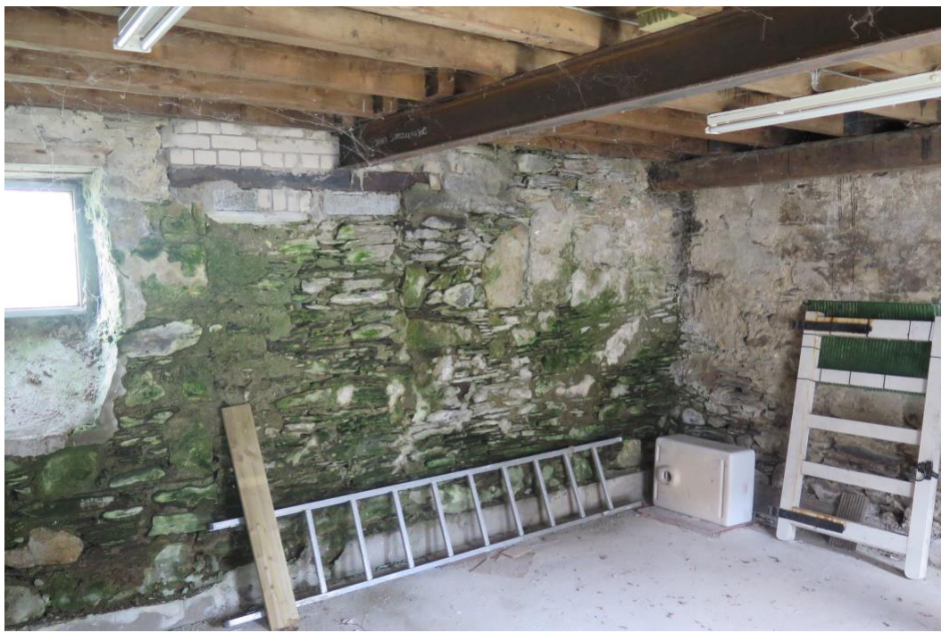 Interior photograph of a stone-walled room with exposed wooden ceiling beams and a steel support beam, showing signs of age and dampness.