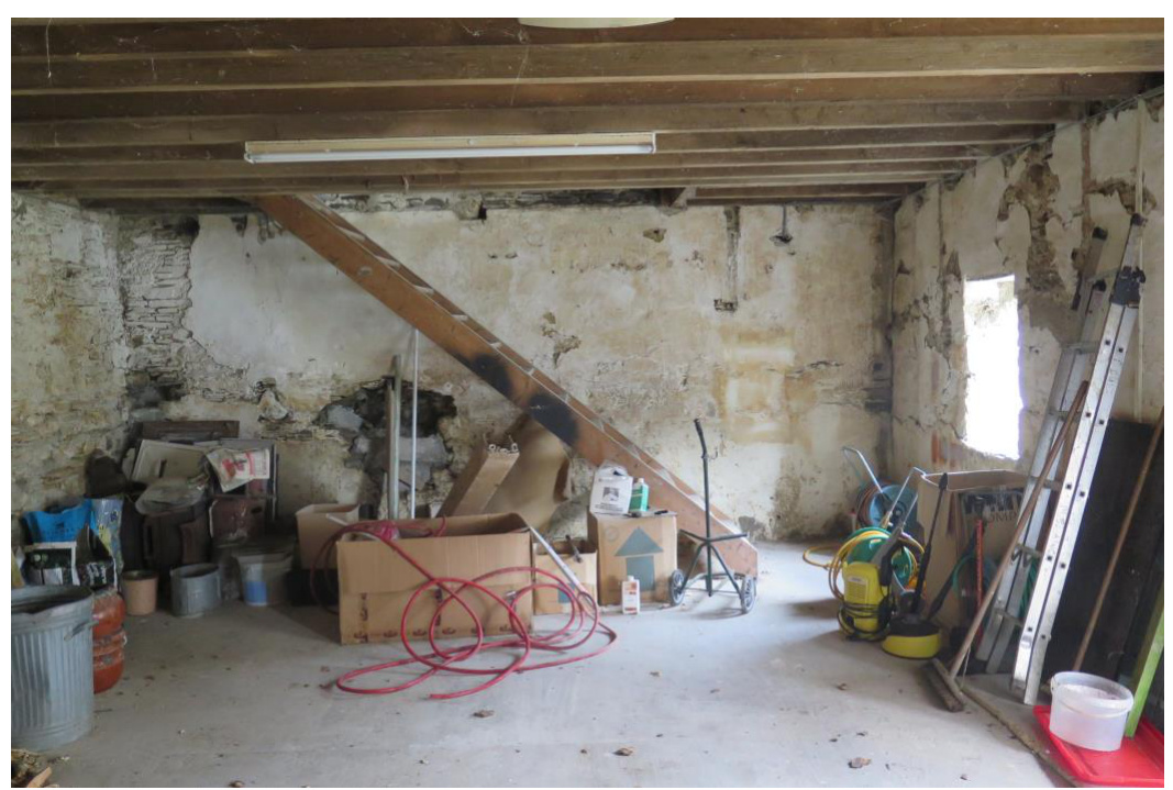 Interior photograph of an existing outbuilding, likely a garage or barn, featuring exposed wooden ceiling beams and rough walls.