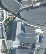 A low-resolution aerial satellite view showing the rooftops of a residential property with solar panels and a driveway containing a car.