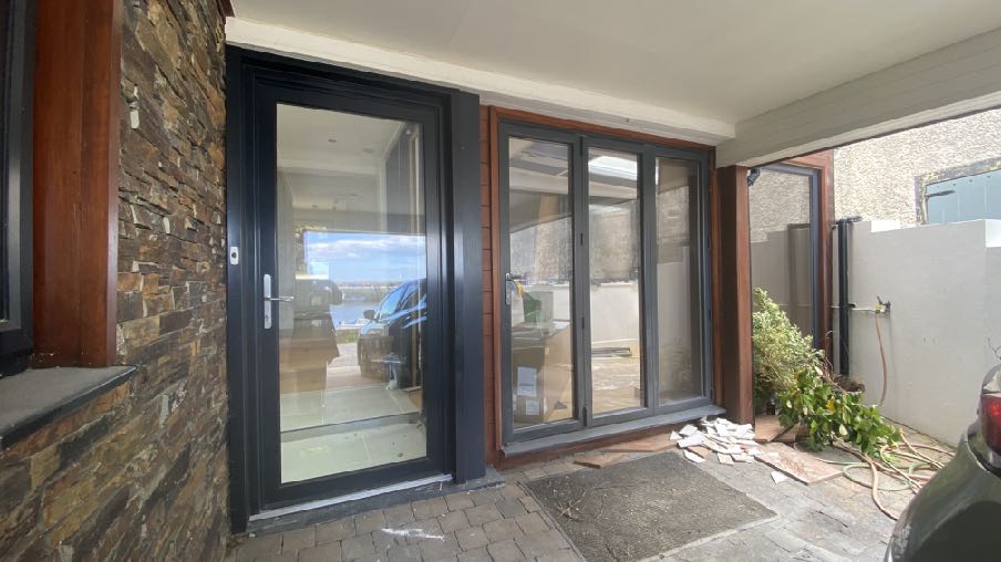 A photograph showing the rear exterior of a property featuring newly installed black-framed patio doors and windows, likely part of a ground floor extension.