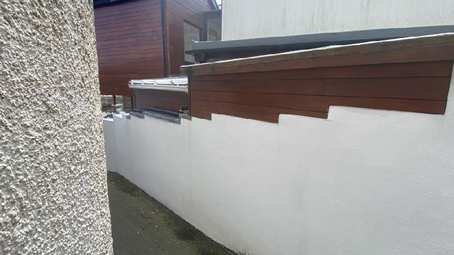 A close-up photograph showing the side elevation of a building featuring white rendered walls and dark brown wooden cladding, likely part of an extension.