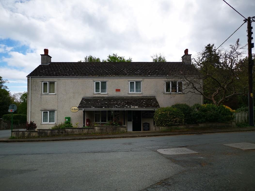 A street-level photograph of a two-story detached building with a slate roof and rendered facade, situated on a roadside corner.