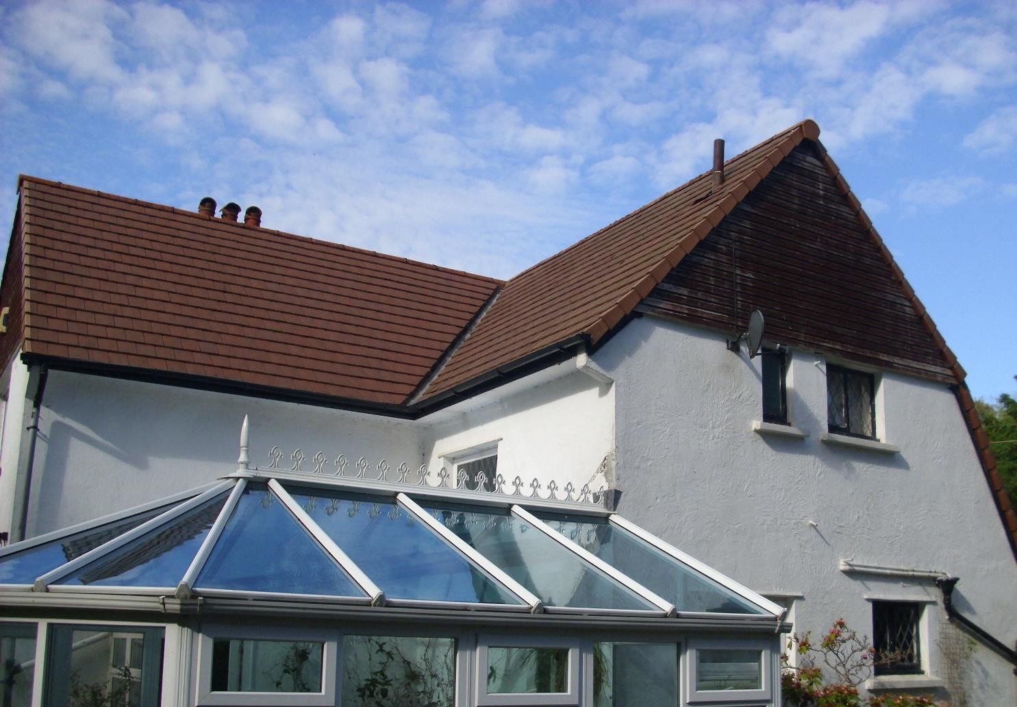 A photograph showing the exterior of a white residential house with a brown tiled roof and a glass conservatory extension.