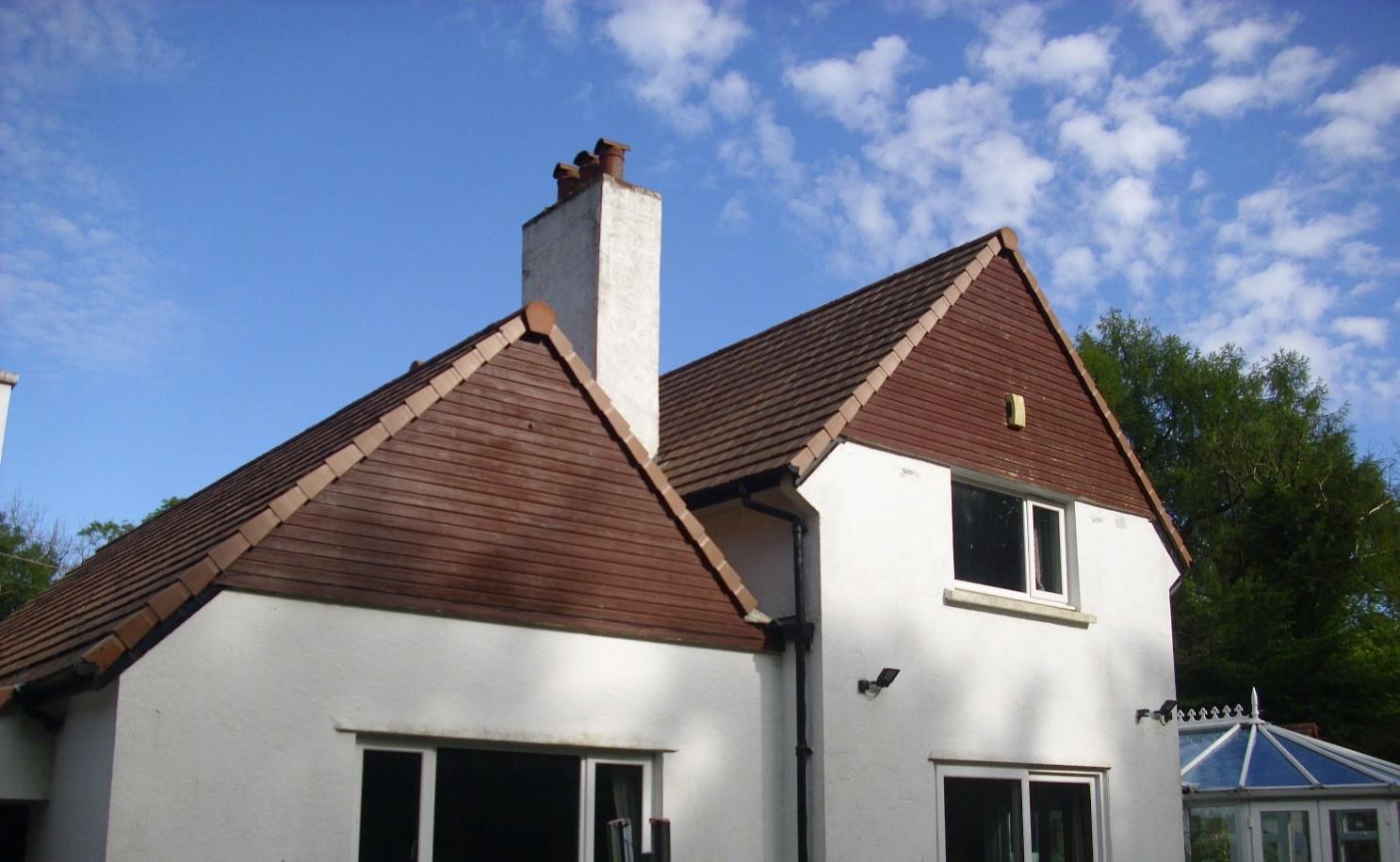 A low-angle exterior photograph of a white residential building featuring a brown tiled roof, a prominent white chimney stack, and a conservatory extension on the right side.