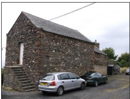 A photograph of a detached stone building with a slate roof and cars parked in front, likely the subject of a planning application for an extension.