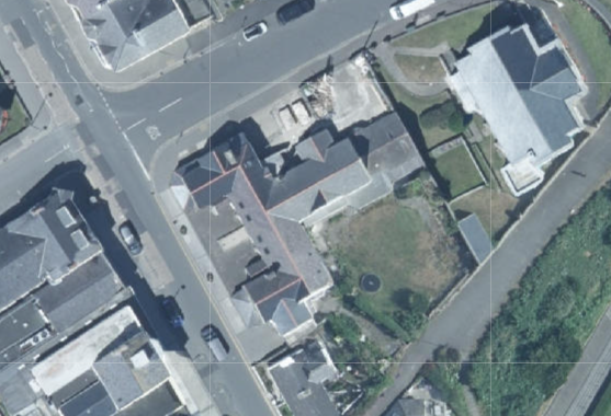 An aerial site plan showing a commercial property complex outlined in red on a street corner, surrounded by other buildings and roads.