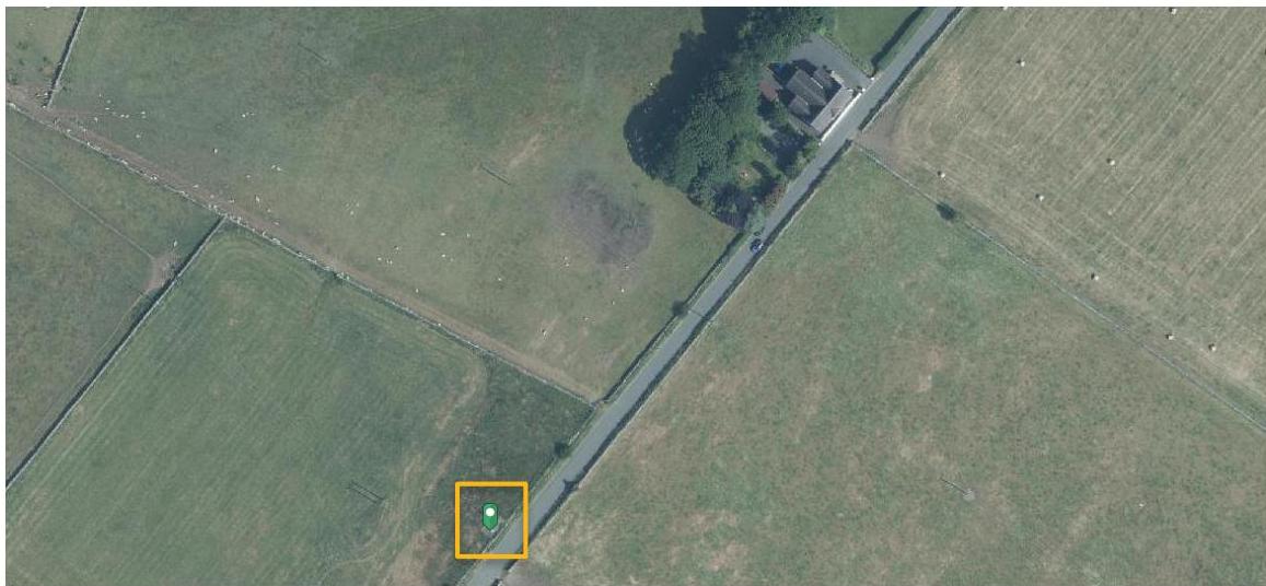An aerial satellite view of a rural landscape showing fields, a road, and a house, with a yellow box highlighting the specific site location for the proposed development.