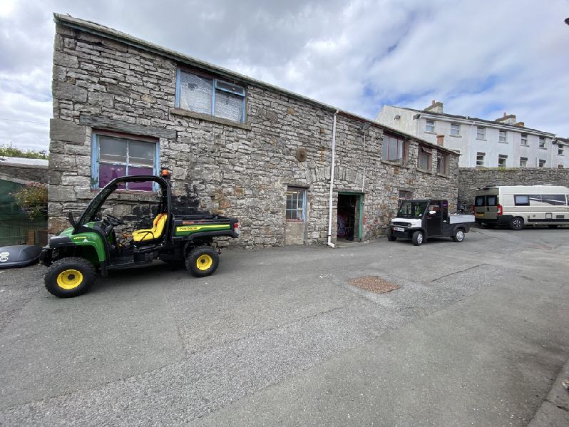 A photograph showing the exterior of a long stone building, identified as Commissioners Yard, with utility vehicles parked in the foreground.