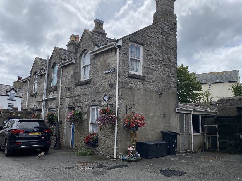 A street-level photograph showing a row of grey stone buildings identified as Commissioners Yard, featuring hanging flower baskets and a parked car.