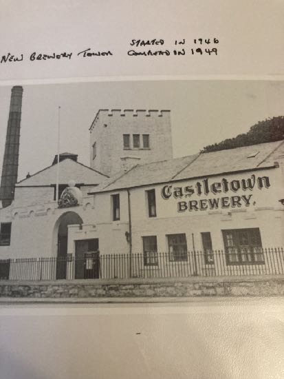 A black and white historical photograph showing the exterior of the Castletown Brewery building with a chimney stack and tower.