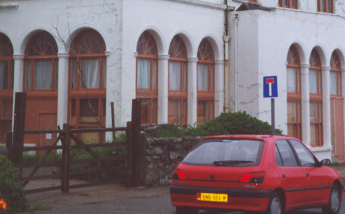 A photograph showing the exterior facade of a white building with distinctive arched windows and a red car parked in the foreground.