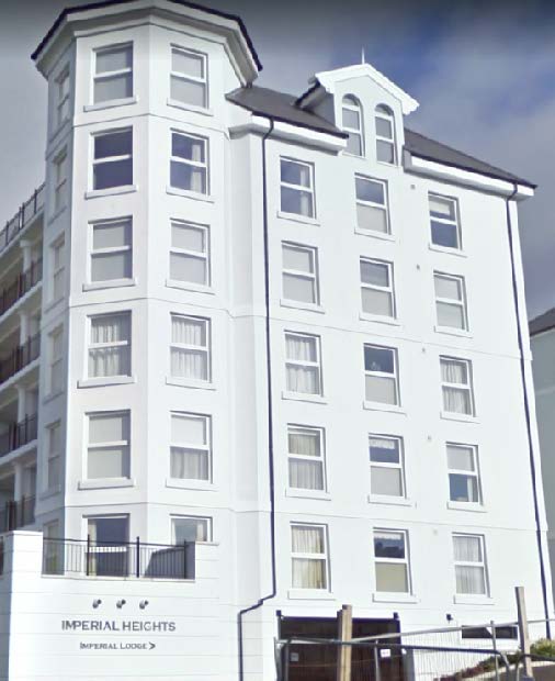 A low-angle photograph of a tall, white multi-story building with a sign reading 'Imperial Heights' at the base, set against a blue sky.