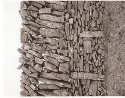 A close-up photograph showing a section of a traditional dry stone wall constructed from stacked flat stones.