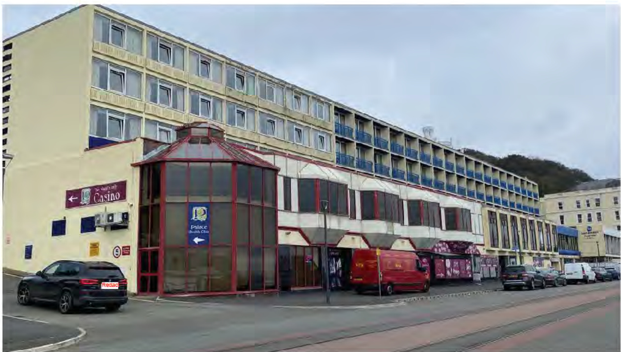 A street-level photograph of a large, multi-story commercial building complex, likely a hotel and casino, featuring a distinctive glass-enclosed entrance structure and signage.