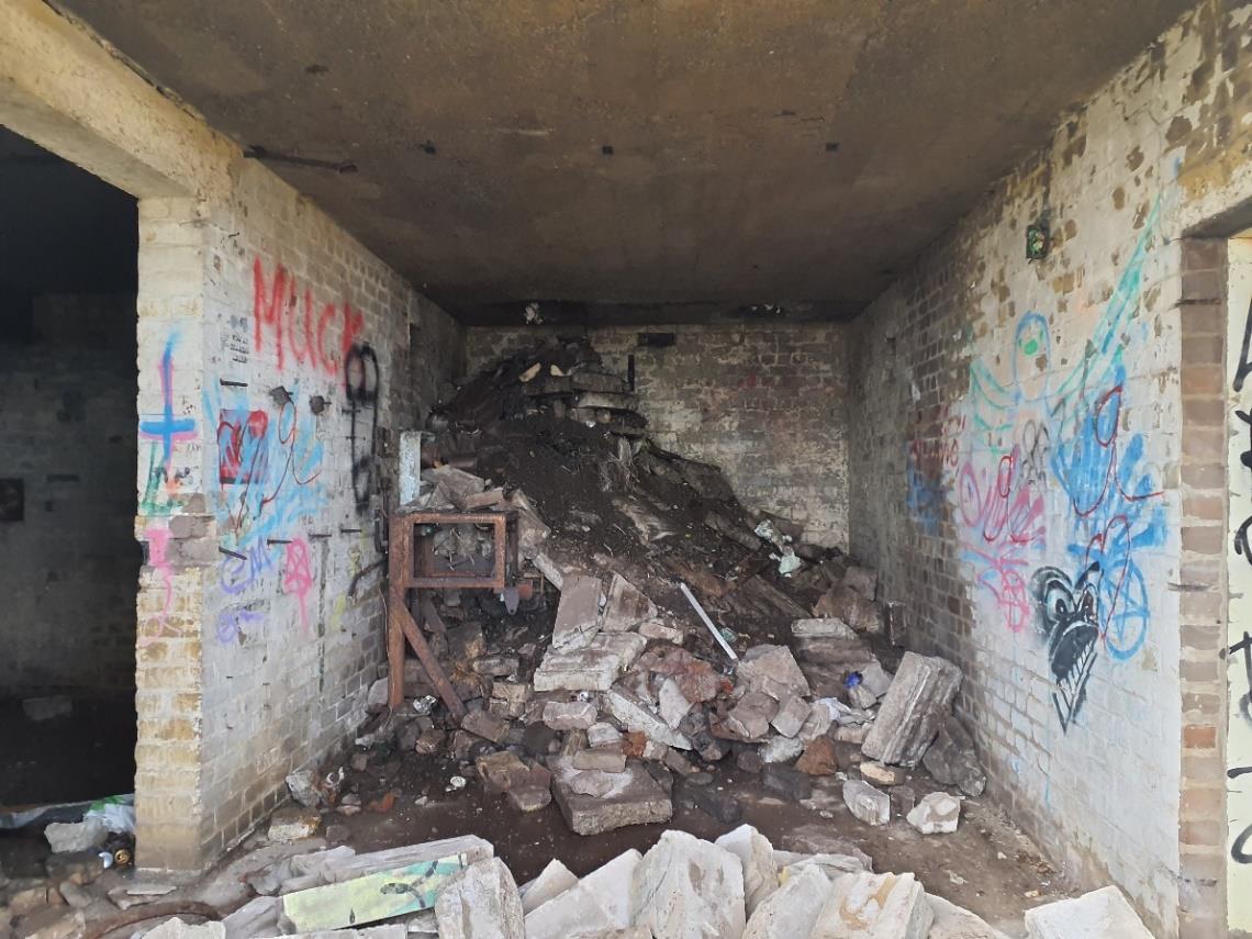 Interior photograph of a dilapidated brick structure filled with a large pile of rubble and debris, with graffiti on the walls.