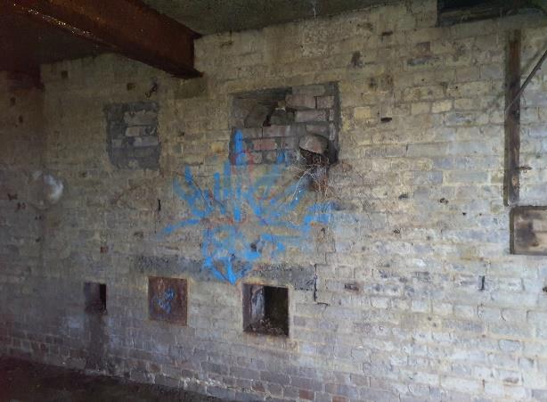 An interior photograph of a weathered brick wall featuring blue spray paint graffiti and several blocked or open apertures.