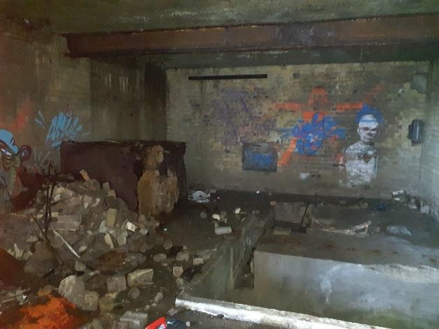 Interior view of a dilapidated brick building with graffiti on the walls and rubble scattered on the floor.