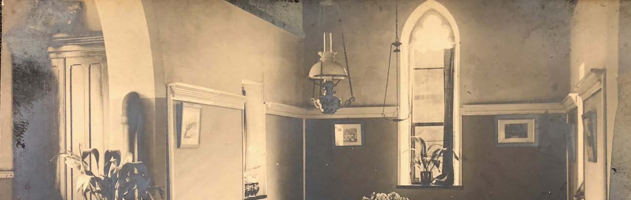 A sepia-toned interior photograph showing a room with a tall, arched lancet window and a hanging light fixture.