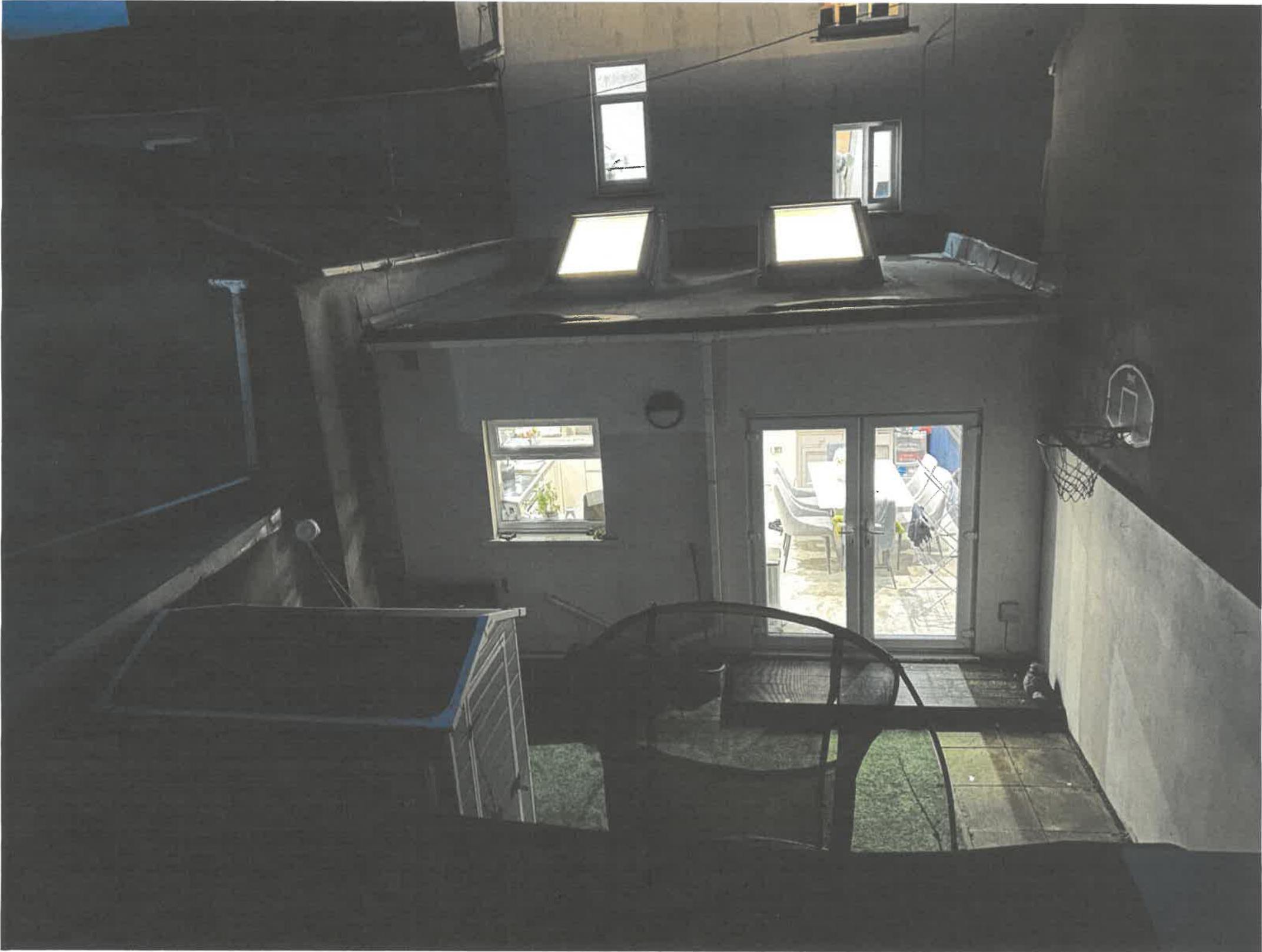 A photograph looking down into a narrow rear courtyard showing a ground floor room with glass doors and a flat roof with skylights.