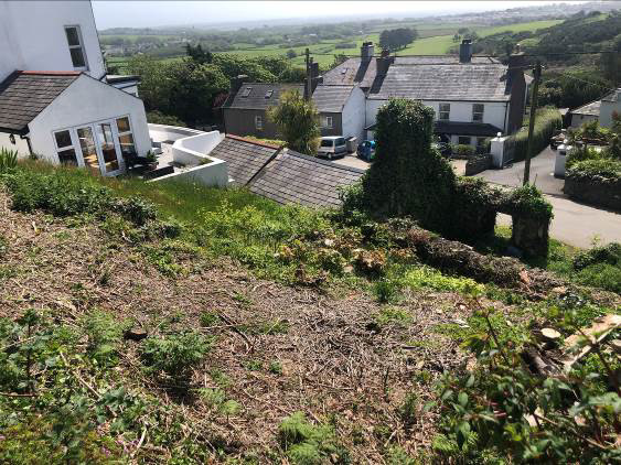 A photograph showing a sloping, cleared plot of land in the foreground, likely the site for the proposed development. In the background, existing residential properties and a rural landscape are visible.