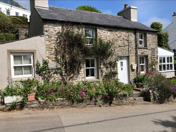 A street-level photograph of an existing two-story stone house with a slate roof and garden, likely showing the current site condition before the proposed development.