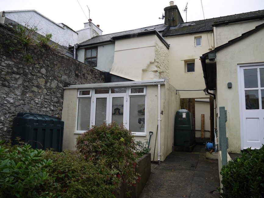 This photograph shows the rear exterior of a residential property, featuring a white conservatory extension attached to a stone and rendered building.