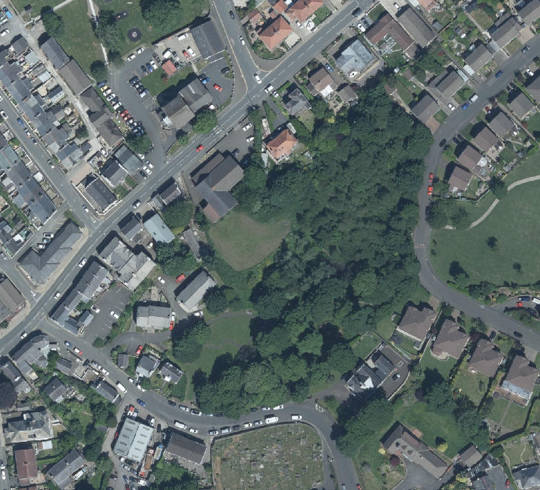 Aerial view of a residential area showing houses, roads, and a central wooded plot.